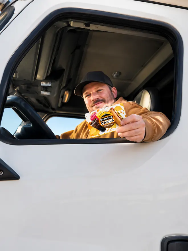 Driver leaning out of his truck cab window holding a Roadside Oasis Rewards card