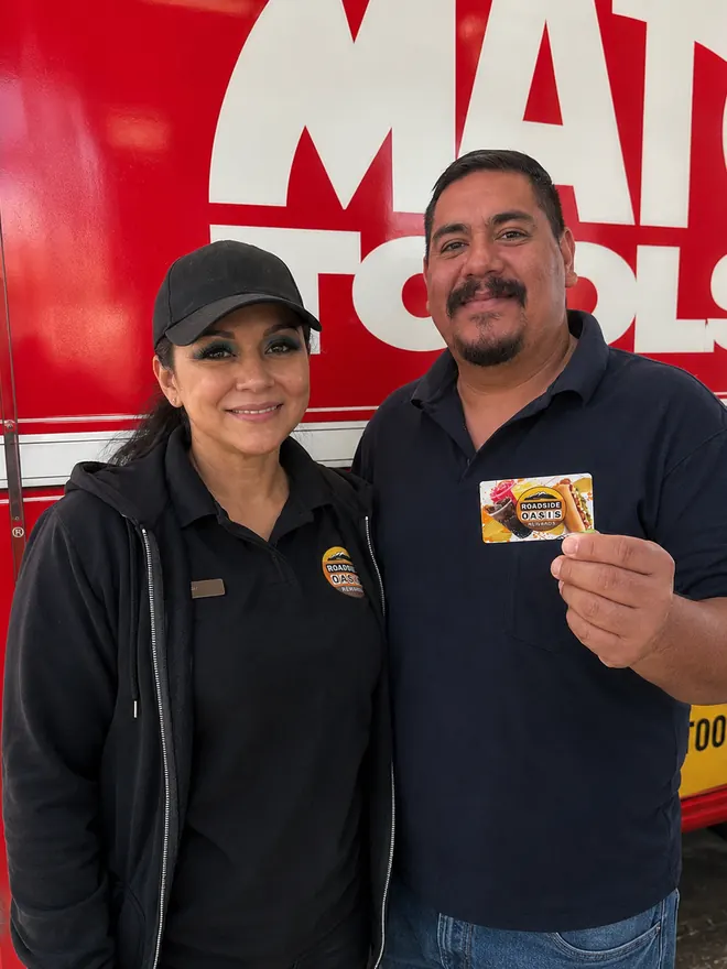 Roadside Oasis team member and a smiling rewards member holding his Rewards card outside the store